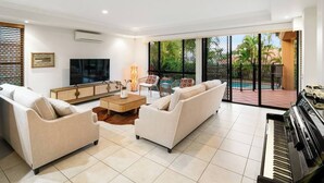 Amplia sala de estar con un piano, sofás, un televisor y un ventanal con vistas a una piscina.