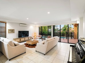 A spacious living room with a piano, sofas, a TV, and a large window overlooking a pool. - Artistic Retreat | Privacy Pool Patio WFH Perfect (Parkinson)