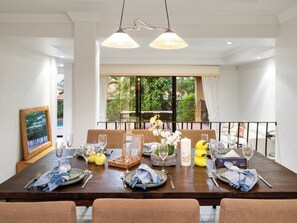 A dining area with a wooden table set for four, two pendant lights, and a view of greenery outside. - Artistic Retreat | Privacy Pool Patio WFH Perfect (Parkinson)