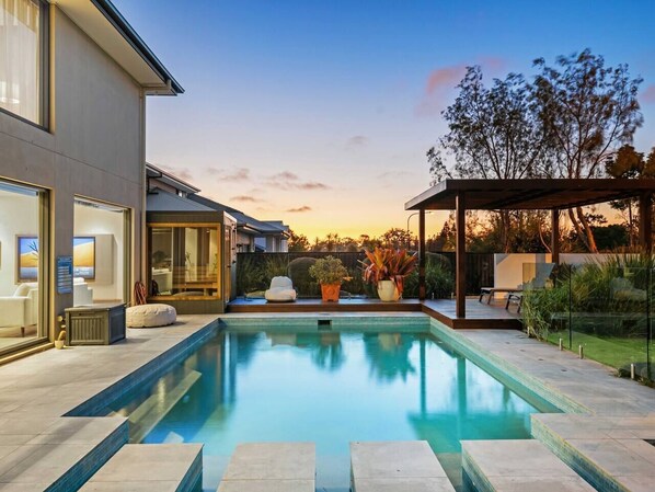 Ein modernes Haus mit Swimmingpool, Sitzgelegenheiten im Freien und einer überdachten Terrasse.