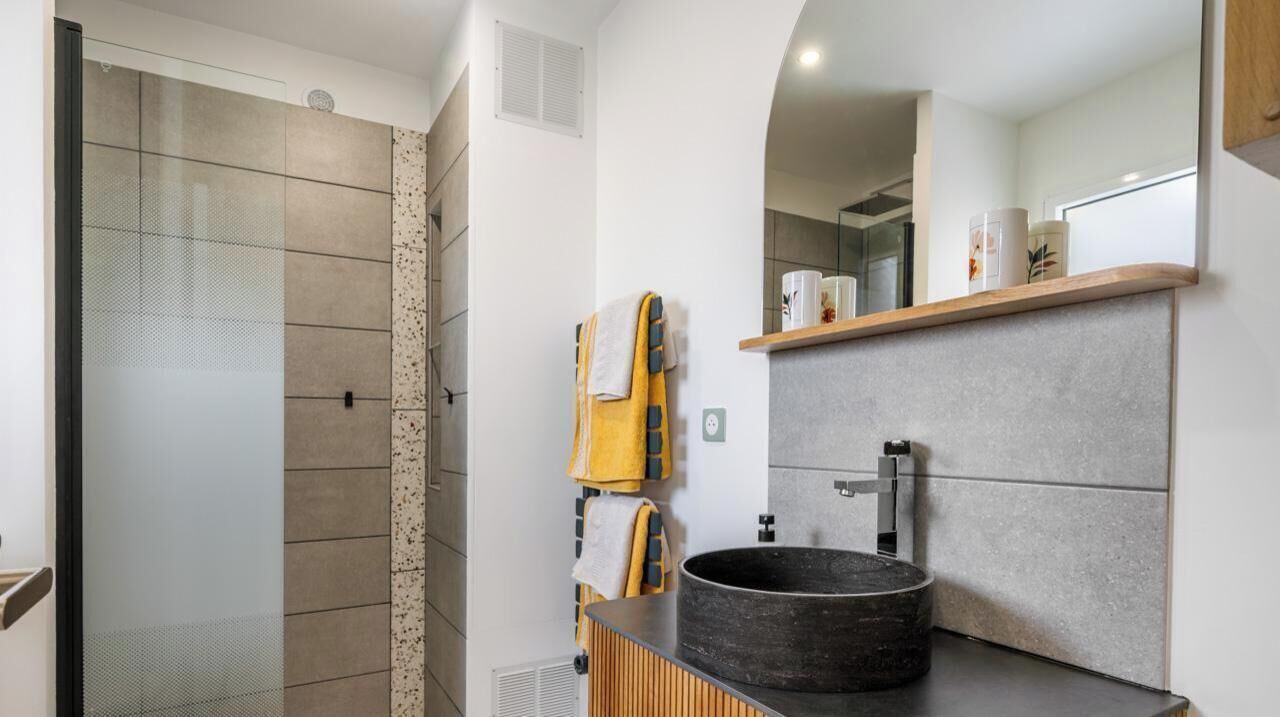 Een moderne badkamer met een douche, een rond wastafel en een spiegel boven het aanrecht.