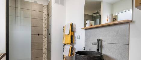 Een moderne badkamer met een douche, een rond wastafel en een spiegel boven het aanrecht.