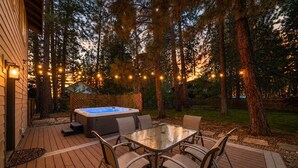 Una terrazza con idromassaggio, tavolo da esterno e sedie, immersa tra alberi e luci decorative.