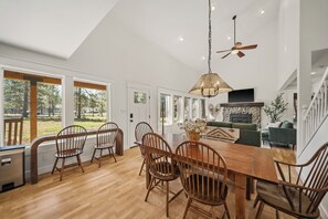 A spacious dining area with a wooden table and chairs, a hanging light fixture, and a fireplace. - HOT TUB, Dog Friendly, Steps from pickleball/pool! (Sisters)