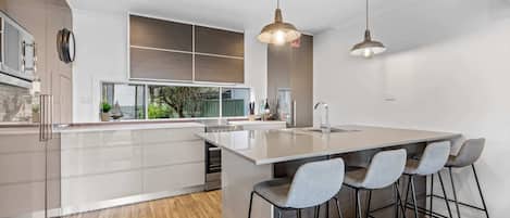Une cuisine moderne dotée d’un grand îlot central, de tabourets de bar, de luminaires suspendus et offrant une vue sur l’extérieur.