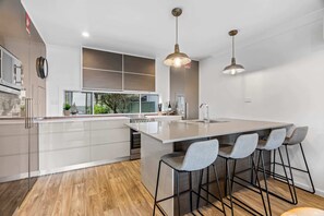 A modern kitchen with a large island, bar stools, pendant lighting, and a view of the outdoors. - Relaxed 2 Bed Coastal Stay Near the Lake (Buff Point)
