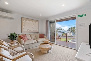 A modern living room with a sofa, chairs, a coffee table, a painting, and a sliding glass door leading to an outdoor area. - Relaxed 2 Bed Coastal Stay Near the Lake (Buff Point)