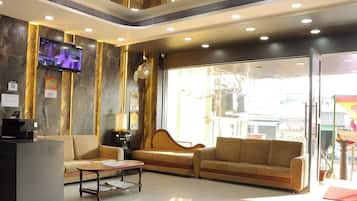 A modern lobby with a reception desk, two sofas, a coffee machine, and a television mounted on the wall.