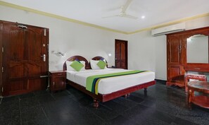 A hotel room with a bed, a nightstand, a wooden wardrobe, a mirror, and a ceiling fan. - OYO 6031 The Waters Edge Beach Resort (Neyyattinkara)