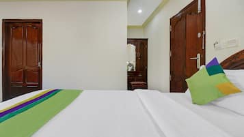 A hotel room with a bed, two wooden doors, a mirror, and a nightstand.