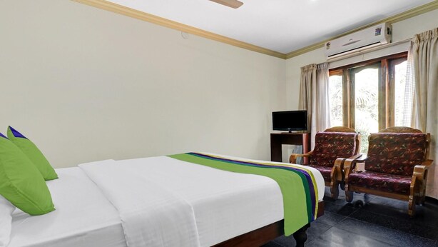 A hotel room with a bed, a television, two chairs, and a window with curtains. - OYO 6031 The Waters Edge Beach Resort (Neyyattinkara)