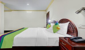 Quarto de hotel com cama, mesa de cabeceira com telefone e espelho.