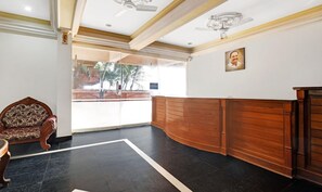 A reception area with a wooden reception desk, a patterned armchair, and a ceiling fan. - OYO 6031 The Waters Edge Beach Resort (Neyyattinkara)