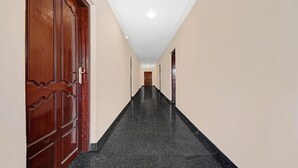 Corredor com porta de madeira à esquerda, chão de azulejos pretos e teto branco.