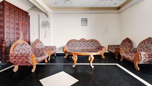 Um quarto com piso de azulejos pretos, uma mesa redonda de madeira e quatro sofás estampados.