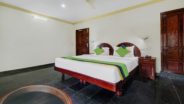 Quarto de hotel com cama, mesa de cabeceira, porta de madeira e ventilador de teto.