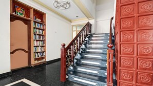 Uma escadaria com corrimão de madeira, uma porta vermelha com painéis decorativos e uma estante cheia de livros.