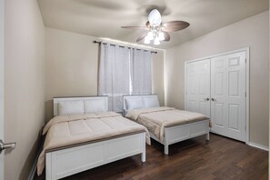Ein Schlafzimmer mit zwei Einzelbetten, einem Deckenventilator, einem Fenster mit Vorhängen und einer weißen Tür.