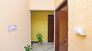Um corredor com parede amarela, porta de madeira e duas plantas em vasos.