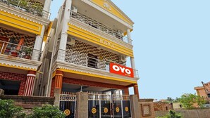Um edifício com vários andares, varandas, um letreiro chamativo da 'OYO' e uma entrada com portão.