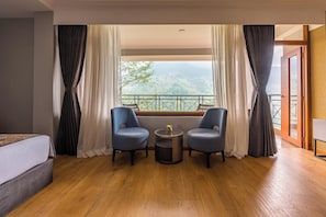 Ein Hotelzimmer mit Bett, zwei Sesseln, einem kleinen Tisch und einem Balkon mit Bergblick.