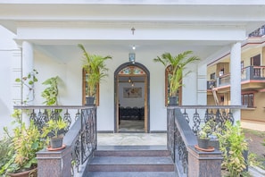 A building entrance with a staircase leading to a door, flanked by potted plants and a railing. - The Sequeira By Madhu And Sons (Majorda)