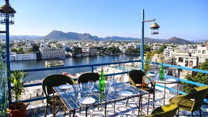 Une terrasse avec une table dressée pour le dîner, offrant une vue sur une rivière et le paysage urbain, avec des montagnes en arrière-plan.