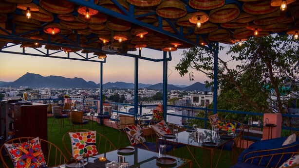 Un espace extérieur aménagé avec des tables et des chaises, offrant une vue sur le paysage urbain et, au loin, sur une montagne.