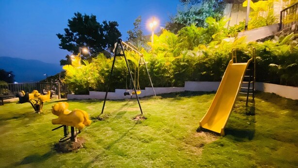 Ein Spielplatz mit Schaukeln und einer Rutsche, umgeben von Gras und Bäumen.