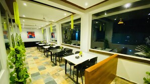 Ein Restaurant mit Tischen, Stühlen, großen Fenstern und Topfpflanzen.