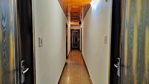 A hallway with a wooden ceiling, white walls, and a tiled floor. - Auckland Hotel And Restaurant (Shimla)