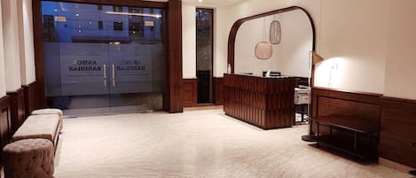 A hotel lobby with a reception desk, seating area, and a large glass door entrance.