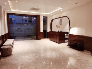 A hotel lobby with a reception desk, seating area, and a large glass door entrance. - Hotel Anmol Bandhan (Jaipur)