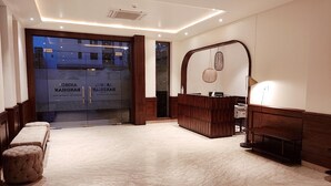 Et hotellobby med reception, siddeområde og stor glasdør.