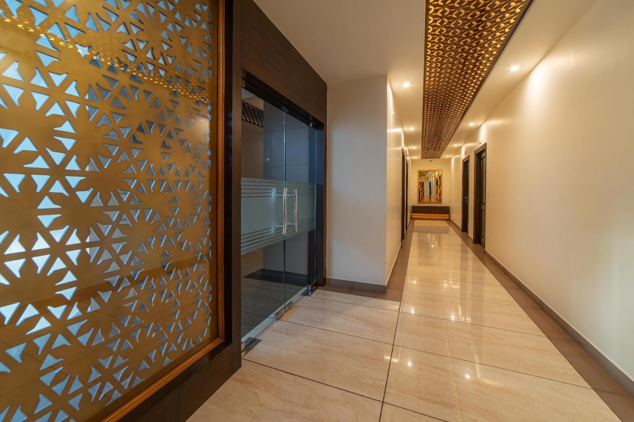 A modern hotel corridor with a patterned wall, glass doors, and a long, well-lit hallway.
