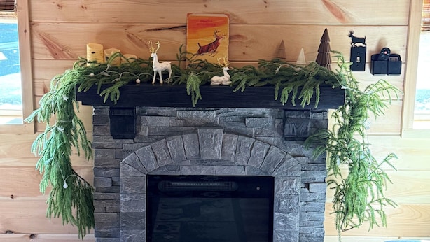 A fireplace with a stone surround, a mounted television above it, and a Christmas decoration with reindeer. - Cabin # 3. Sammy’s Deer Den  (Lima)