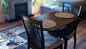 A cozy cabin interior with a fireplace, a television mounted on the wall, a dining table with chairs, and a sofa in the background. - Cabin # 3. Sammy’s Deer Den  (Lima)