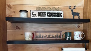 A kitchen with a sink, a coffee maker, a mug, a framed picture, and a shelf with a deer silhouette and a sign. - Cabin # 3. Sammy’s Deer Den  (Lima)