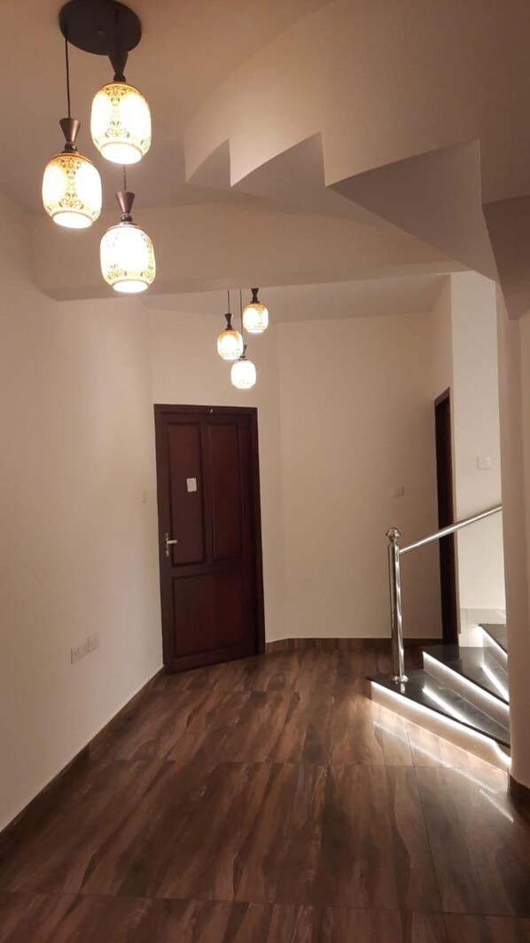 Un pasillo con piso de madera, una puerta de madera oscura y una escalera con barandilla de metal.