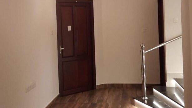 Um corredor com piso de madeira, uma porta de madeira escura e uma escada com guarda-corpo de metal.
