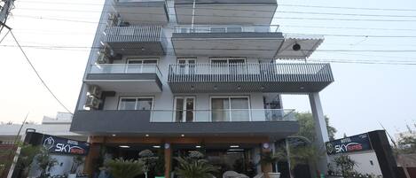 A multi-story hotel with balconies, a covered entrance, and potted plants.