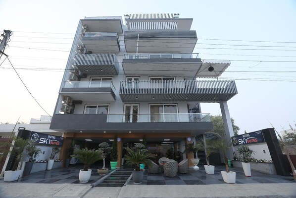 A multi-story hotel with balconies, a covered entrance, and potted plants. - Sky Suites (Gurugram)