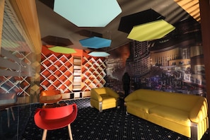 A modern interior with geometric shelving, a red chair, yellow sofas, and a cityscape mural. - Sky Suites (Gurugram)