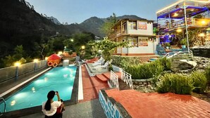 A hotel with a swimming pool, a guest taking a photo, and a mountain backdrop.