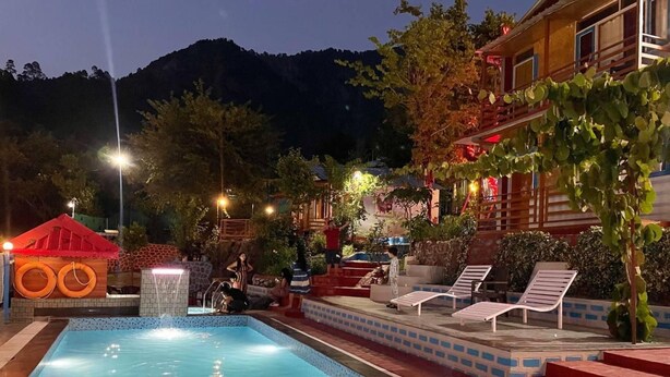 A swimming pool with steps leading to a terrace, surrounded by trees and a mountain in the background.
