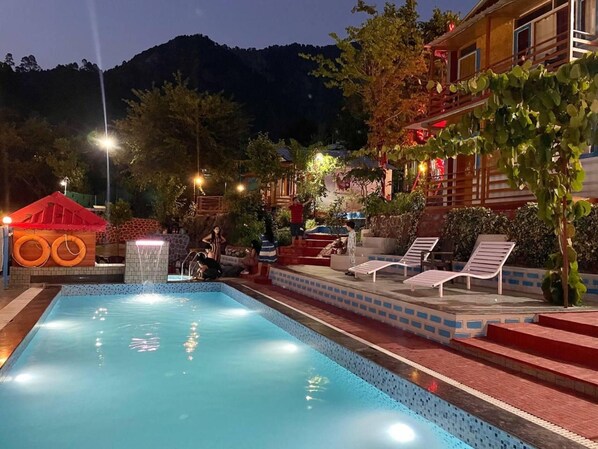 A swimming pool with steps leading to a terrace, surrounded by trees and a mountain in the background.