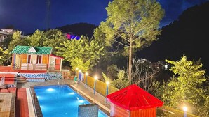 A swimming pool with a red-roofed structure nearby, surrounded by trees and a night sky.