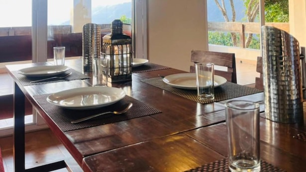Un comedor con una mesa de madera dispuesta para cuatro, un farol y un cuadro en la pared.