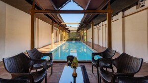 Uma área de piscina coberta com cadeiras e uma mesa, vista clara da piscina e uma estrutura de pérgula.
