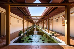 A corridor with a central water feature, potted plants, and traditional architectural elements.